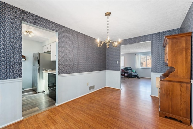 unfurnished dining area featuring wallpapered walls, visible vents, wood finished floors, and wainscoting