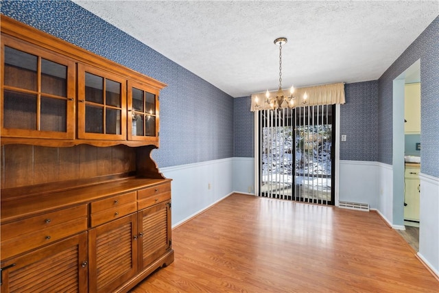 unfurnished dining area with wainscoting, visible vents, and wallpapered walls