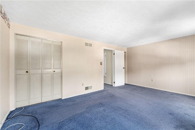 unfurnished bedroom with wallpapered walls, carpet, and visible vents