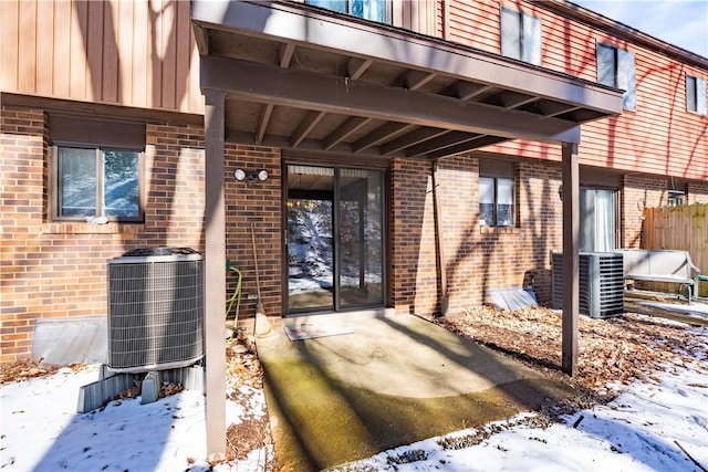 snow covered property entrance with cooling unit and brick siding