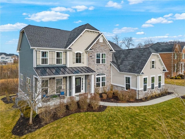 craftsman-style home featuring covered porch, a shingled roof, stone siding, a front lawn, and a standing seam roof