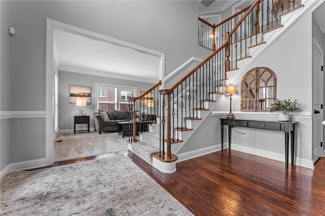 entryway with baseboards, a towering ceiling, stairway, ornamental molding, and wood finished floors