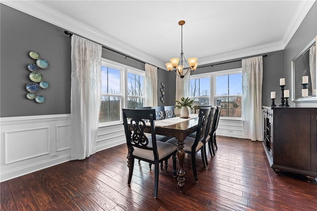 dining area featuring a chandelier, a decorative wall, dark wood-style flooring, ornamental molding, and wainscoting