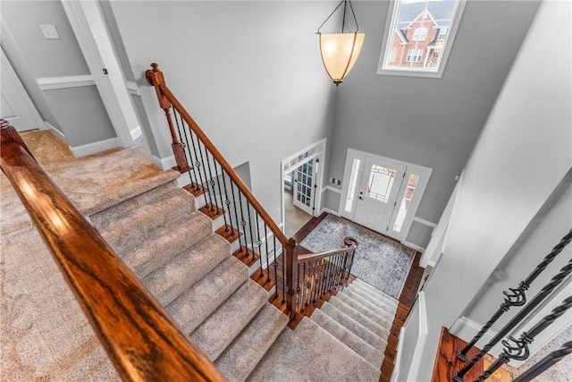 staircase featuring baseboards, a healthy amount of sunlight, and a high ceiling