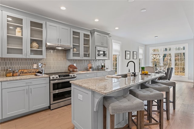 kitchen featuring gray cabinetry, appliances with stainless steel finishes, a sink, under cabinet range hood, and a kitchen breakfast bar