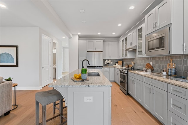 kitchen with stainless steel appliances, a sink, a kitchen breakfast bar, light wood finished floors, and tasteful backsplash