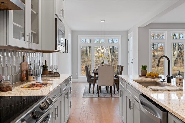 kitchen with light wood finished floors, appliances with stainless steel finishes, light stone countertops, under cabinet range hood, and a sink