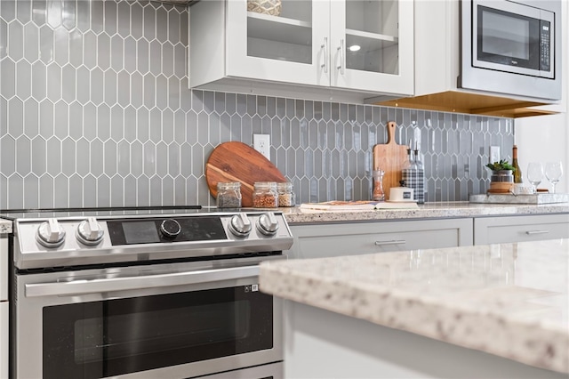 kitchen with backsplash, glass insert cabinets, white cabinets, stainless steel range with electric stovetop, and built in microwave