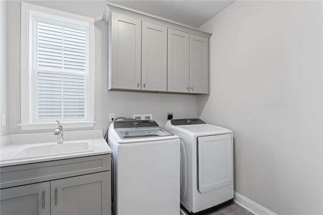 washroom with cabinet space, baseboards, washer and dryer, and a sink