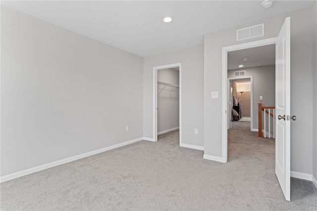 unfurnished bedroom featuring visible vents, light carpet, baseboards, and a spacious closet