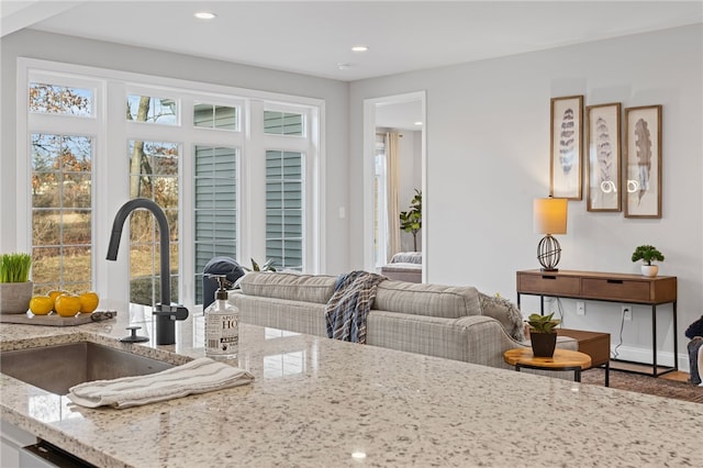 kitchen featuring open floor plan, light stone counters, a sink, and recessed lighting