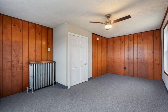 carpeted empty room with wood walls, ceiling fan, and a textured ceiling