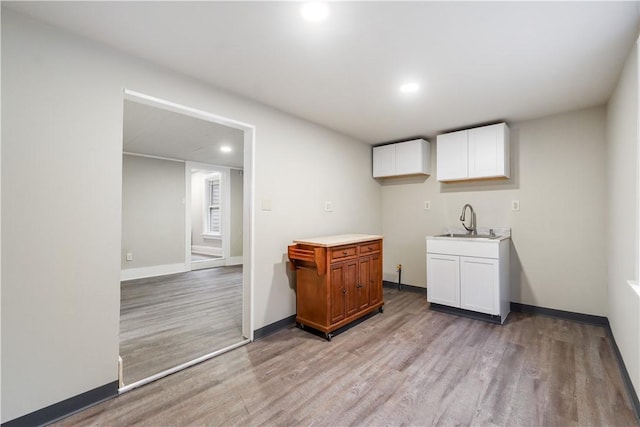 kitchen featuring baseboards, white cabinets, light wood-type flooring, a sink, and recessed lighting