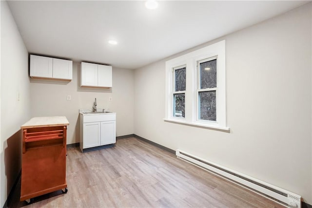 clothes washing area with baseboards, a baseboard radiator, a sink, and light wood-style floors