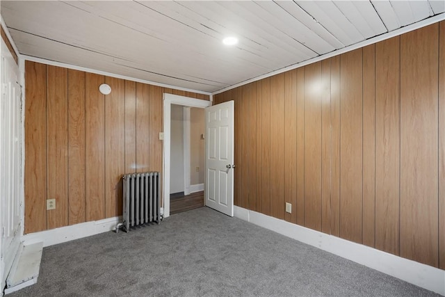 unfurnished room with radiator, carpet flooring, and wood walls