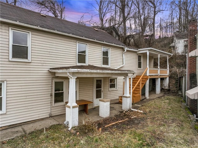 back of property at dusk featuring a patio area, stairway, and roof with shingles