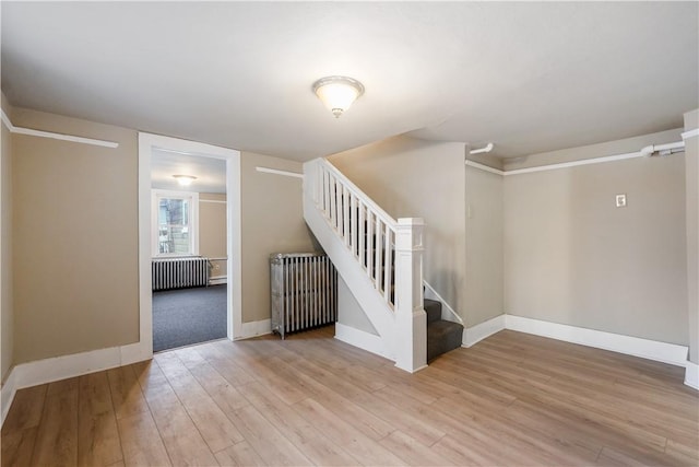 spare room with baseboards, stairway, light wood-style flooring, and radiator