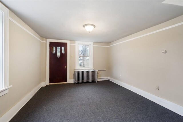 foyer entrance with radiator, dark carpet, and baseboards