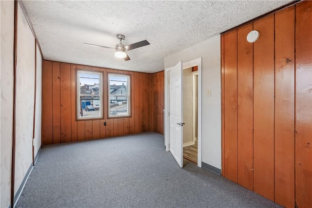 unfurnished bedroom featuring baseboards, a ceiling fan, a textured ceiling, carpet flooring, and wood walls