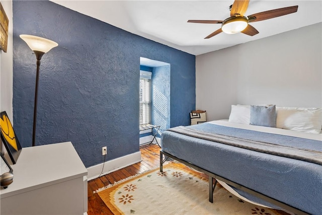 bedroom featuring ceiling fan, a textured wall, hardwood / wood-style floors, and baseboards