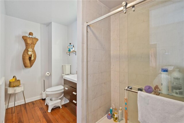 bathroom featuring a stall shower, baseboards, toilet, wood finished floors, and vanity