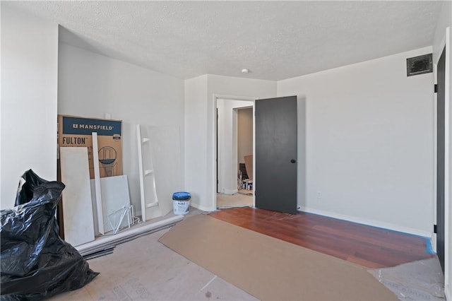 bedroom with a textured ceiling, wood finished floors, visible vents, and baseboards