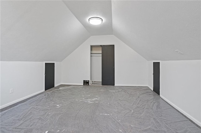 additional living space featuring vaulted ceiling, a textured ceiling, and baseboards