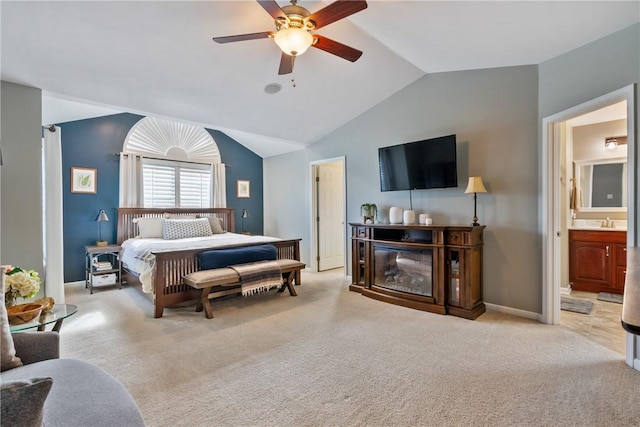 carpeted bedroom with vaulted ceiling, a glass covered fireplace, ensuite bath, and baseboards