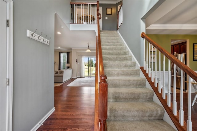 staircase with baseboards, a towering ceiling, wood finished floors, crown molding, and recessed lighting