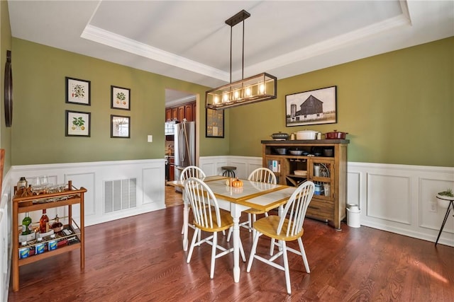 dining room featuring a tray ceiling, dark wood-type flooring, wainscoting, and visible vents