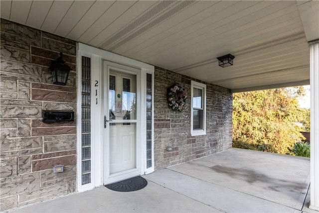 doorway to property featuring a porch and brick siding