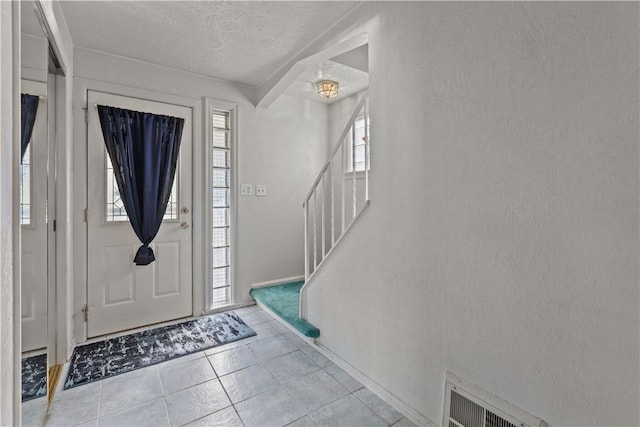 entryway featuring a textured ceiling, a textured wall, visible vents, stairs, and tile patterned floors