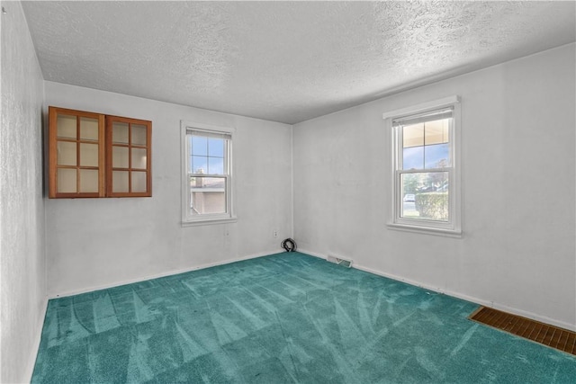 carpeted empty room with a healthy amount of sunlight, baseboards, visible vents, and a textured ceiling