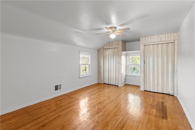 unfurnished bedroom with wood-type flooring, visible vents, vaulted ceiling, and baseboards