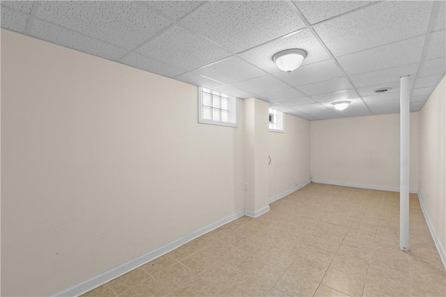 basement with a paneled ceiling and baseboards