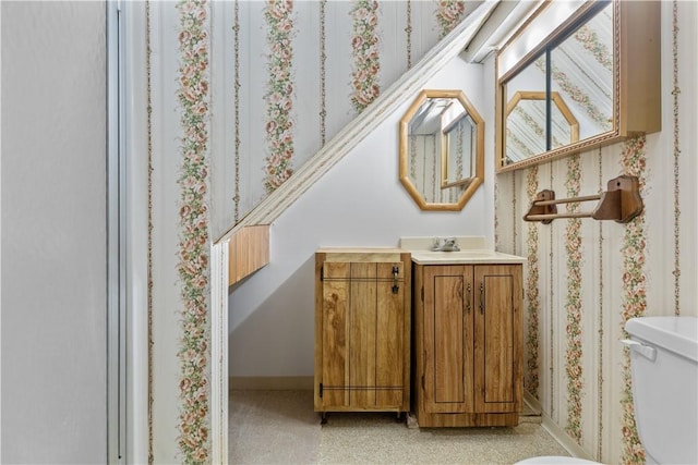 bathroom featuring baseboards, vanity, toilet, and wallpapered walls