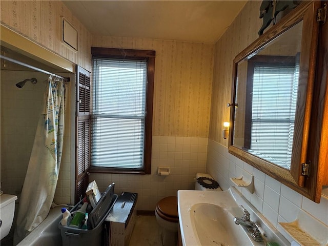 bathroom with wallpapered walls, toilet, a wainscoted wall, shower / tub combo with curtain, and tile walls