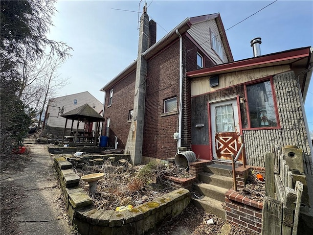 view of front facade featuring entry steps, a gazebo, brick siding, and a chimney