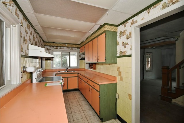 kitchen featuring custom range hood, electric range, wainscoting, a sink, and wallpapered walls