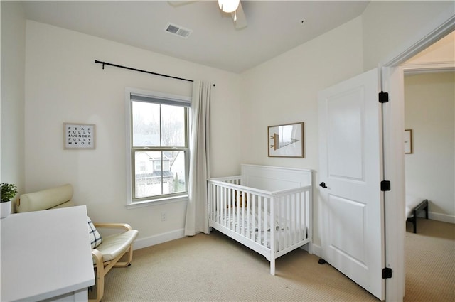 bedroom with visible vents, a ceiling fan, light carpet, a nursery area, and baseboards