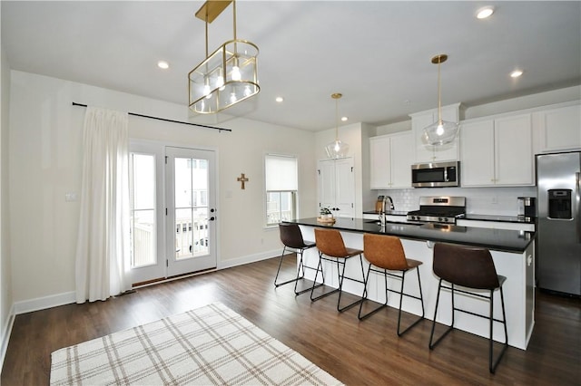 kitchen with decorative backsplash, dark countertops, appliances with stainless steel finishes, a kitchen bar, and a sink