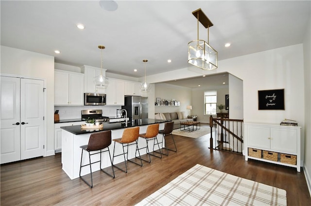 kitchen with a breakfast bar, dark wood-style flooring, stainless steel appliances, open floor plan, and a kitchen island with sink