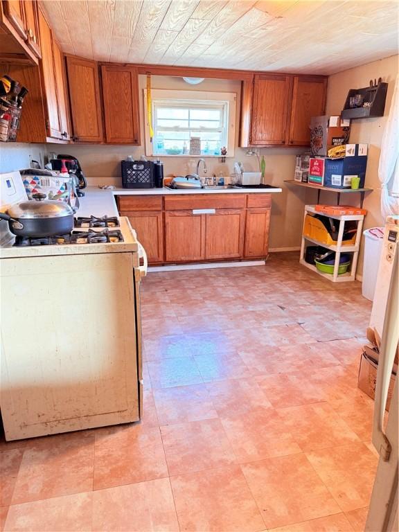 kitchen featuring white gas range oven, brown cabinetry, a sink, and light countertops