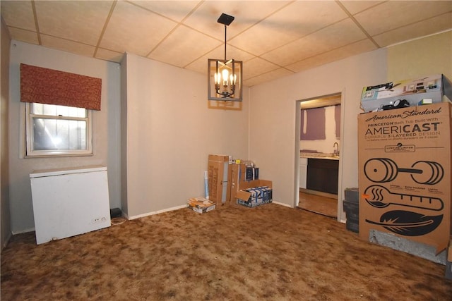 unfurnished dining area featuring baseboards, carpet flooring, a drop ceiling, and an inviting chandelier