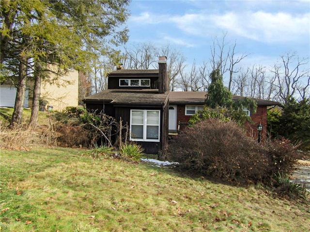 rear view of house featuring brick siding, a chimney, and a yard