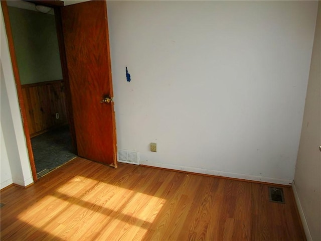 empty room with wood finished floors, visible vents, and baseboards