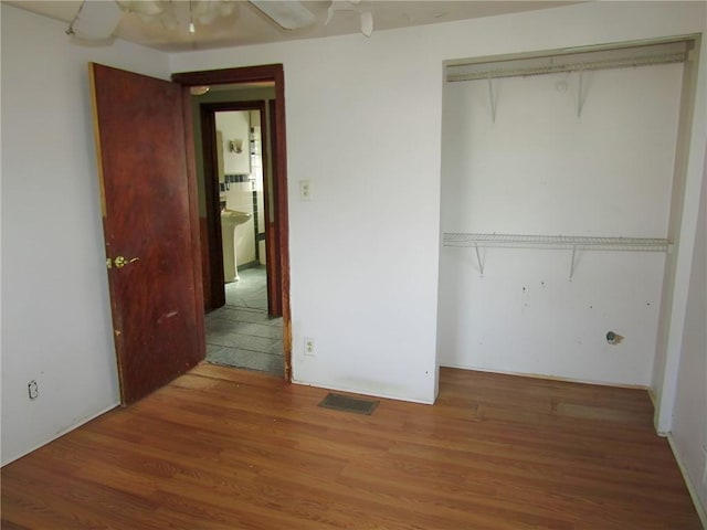 unfurnished bedroom with ceiling fan, a closet, wood finished floors, and visible vents