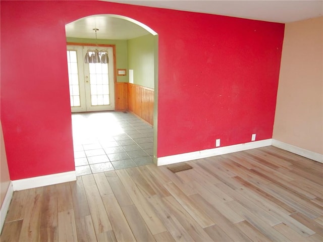 unfurnished room with arched walkways, a notable chandelier, a wainscoted wall, wood finished floors, and baseboards