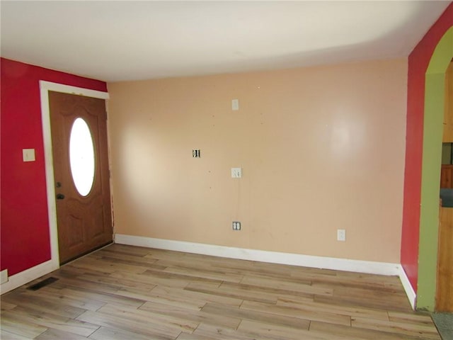 entrance foyer featuring light wood-type flooring, visible vents, arched walkways, and baseboards