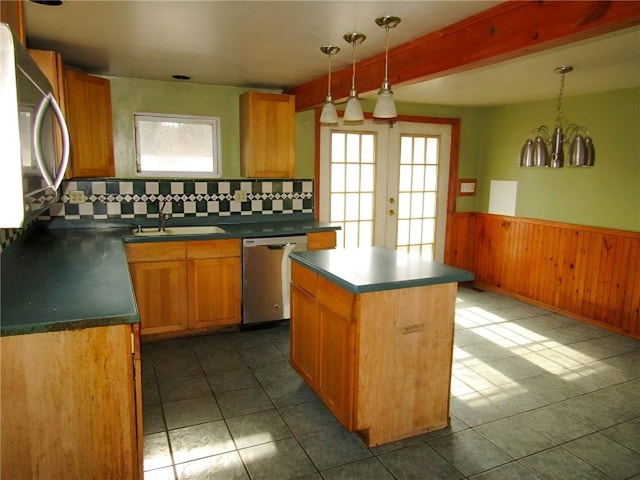 kitchen featuring a wainscoted wall, a kitchen island, a sink, appliances with stainless steel finishes, and dark countertops